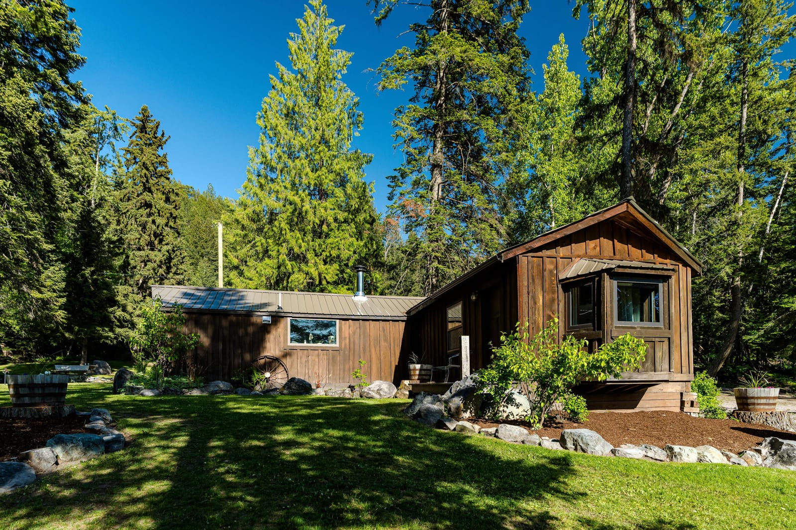 The cabin from the lawn — dark wood siding, peaked roof, tall evergreens behind