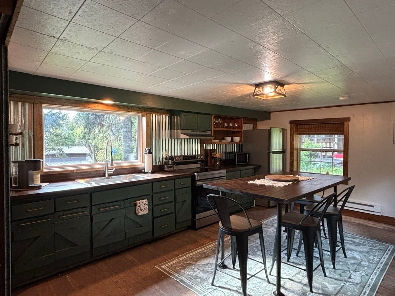 Open kitchen with deep-green cabinetry and a rustic farmhouse dining table